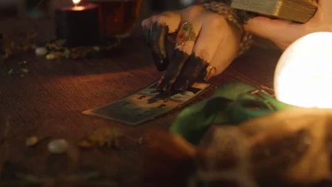 Fortune teller's hands with dark fingers reading a tarot card on a wooden table, Stock Footage 318869278