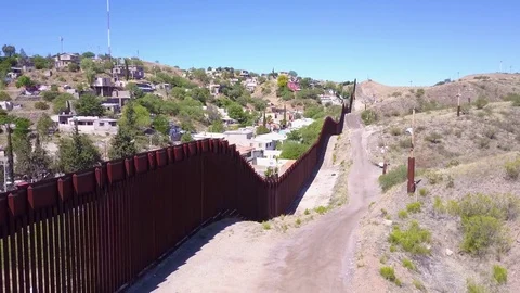 Forward aerial along the U.S Mexican border wall fence reveals the town of Stock Footage 79399863