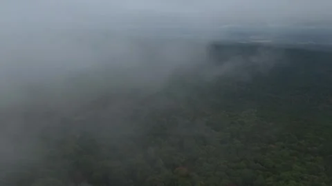 Forward aerial flight through low clouds over a forested mountain valley along Stock Footage 347075608