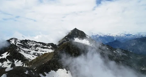 Forward aerial top view over cloudy rocky snowy mountain in sunny day with Stock Footage 93205006