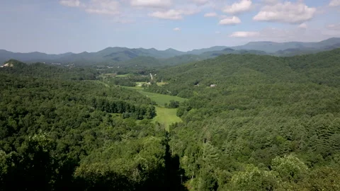 Forward aerial track over forested mountains and farmland Stock Footage 247978333