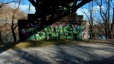 Forward dolly moving under iron railway bridge pillar with SPLASH graffiti Stock Footage 123927682