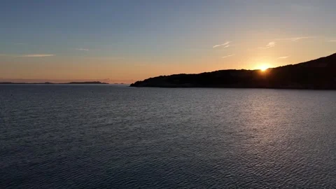 Forward Drone Flight Along Quiet Sunrise Coast with Sun Emerging Behind 库存影片 334854515