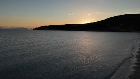 Forward Drone Flight Toward Sun Rising Behind Hill Over Tranquil Beach Vídeo Stock 334796991