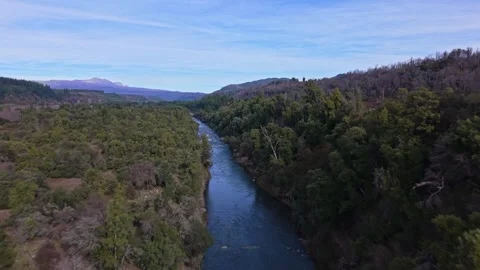 Forward flight over a calm blue river winding through a dense forested valley Видео 347884976