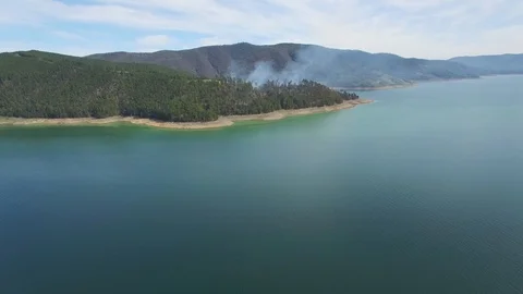 Forward flight over lake towards smoke rising from forest on the coastline Stock Footage 96695845