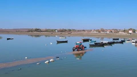 Forward move over a tractor and fishing boats on a lake with migratory pelicans Stock Footage 119600750