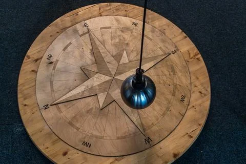 Foucault pendulum ball hanging over a wooden compass rose on exhibition. Th.. Stock Photos