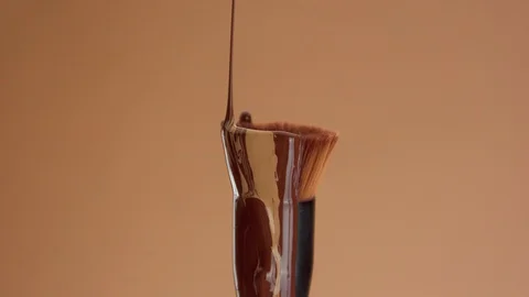 A foundation brush with a liquid foundation for deep skin tones covering it and Stock Footage 128630100