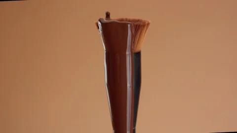 A foundation brush with a liquid foundation for deep skin tones covering it Stock Footage 128630556