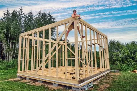 Foundation on concrete blocks supports frame house, young worker uses cordl.. Stock Photos