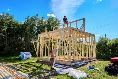 Foundation on concrete blocks supports frame house, two workers lift lumber.. Stock Photos