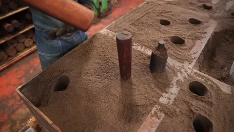 Foundry worker inserting cylindrical core pins into a sand casting mold by hand Stock Footage 343875826