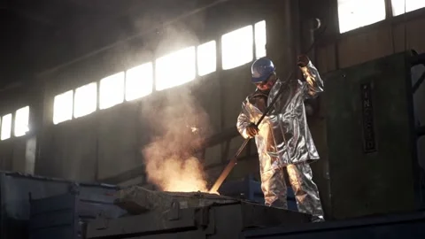 In the foundry, a worker in protective clothing stirs the molten metal in the fu Stock Footage 146637140