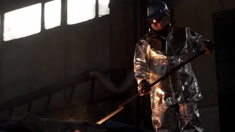 In the foundry, a worker in protective clothing stirs the molten metal in the fu Stock Footage 146637247