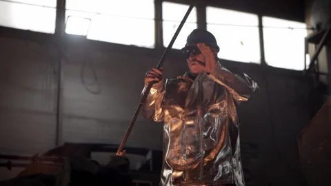 In the foundry, a worker in protective clothing stirs the molten metal in the fu 스톡 동영상 146637357