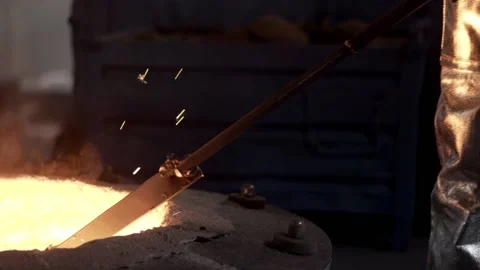 In the foundry, a worker in protective clothing stirs the molten metal in the fu Stock Footage 146836666