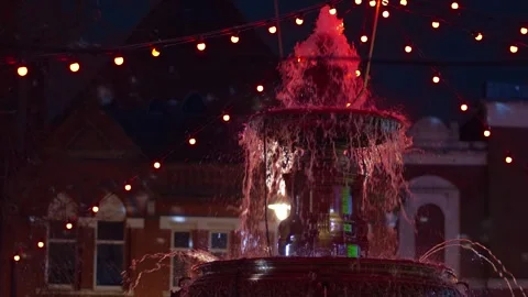 Fountain glowing under festive string lights at night, water streaming down in Stock Footage 303168594