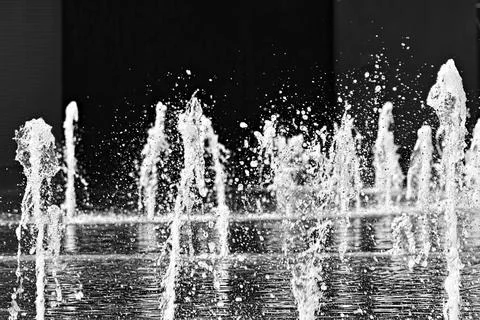 Fountain water jets rise dynamically against dark background Stock Photos