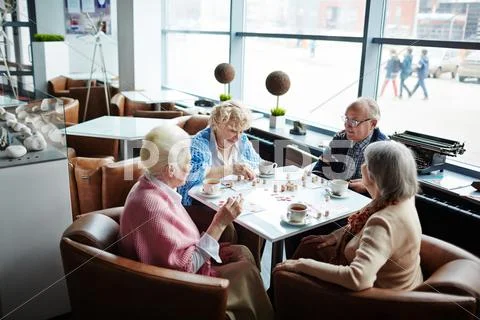 Four aged people sitting in cafe at leisure and playing lotto Stock Photos