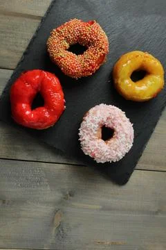 Four appetizing glazed doughnuts: red, white, yellow with sprinkles on a gr.. Stock Photos