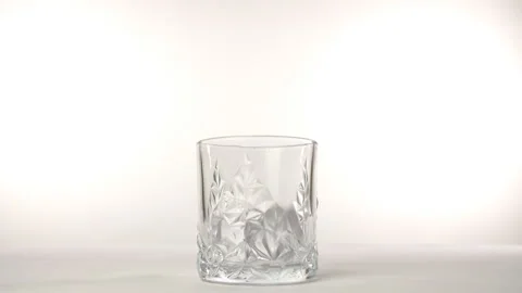 Four big ice cubes dropped in an empty glass of whiskey against a white backg... 스톡 동영상 154679560