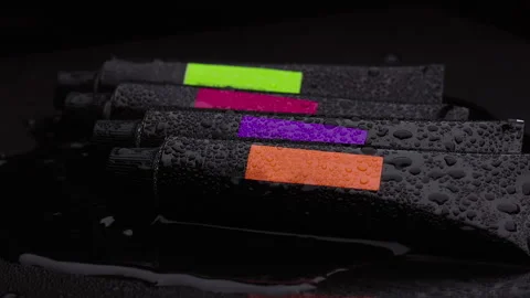 Four black plastic tubes with colored labels lie on a wet dark table Vidéo 267454216