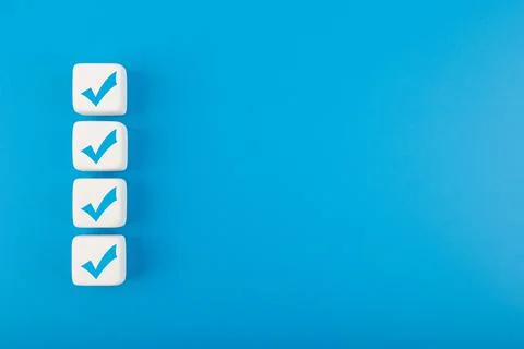 Four blue checkmarks on white cubes in a row against blue background with copy Stock Photos