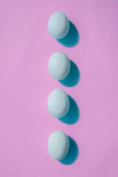 Four blue eggs lie in a row like a spine. The eggs cast a blue shadow. Stock Photos