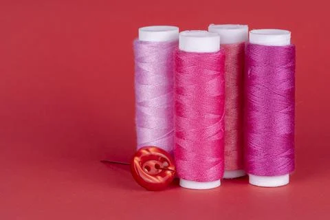 Four bobbins of sewing thread of different shades of pink with a red button a Stock Photos
