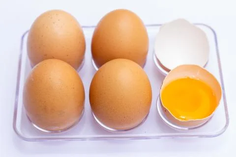 Four brown eggs lay on an egg tray with an eggshell on a white background. Th Stock Photos