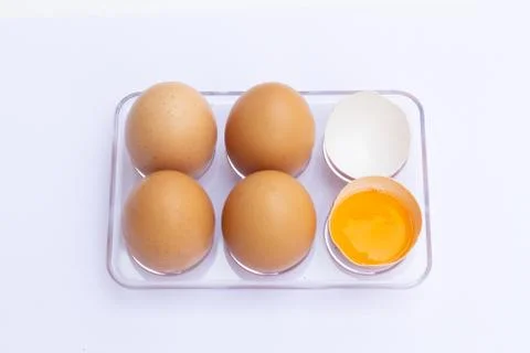 Four brown eggs lay on an egg tray with an eggshell on a white background. Stock Photos