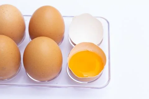 Four brown eggs lay on an egg tray with an eggshell on a white background. Th Stock Photos
