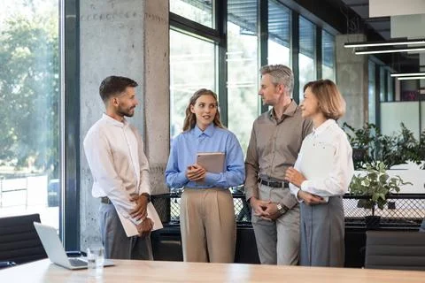 Four business professionals using laptop on desk discussing strategy company Stock Photos