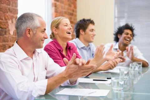 Four businesspeople in boardroom applauding and smiling Stock Photos
