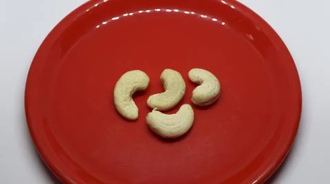 Four cashew nuts is on a white background on a red plate Stock Photos