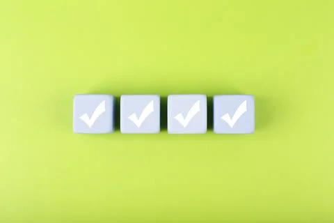 Four checkmarks on white cubes against bright green background Stock Photos