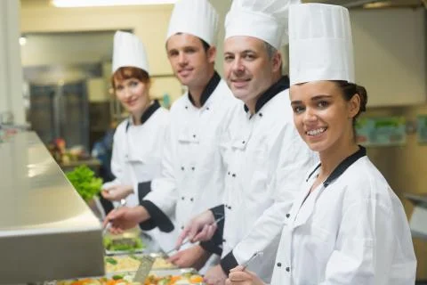 Four chefs smiling at camera while working at serving trays Stock Photos