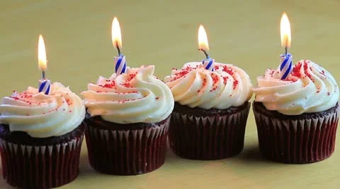 Four chocolate birthday cupcakes lined up with one lit blue candle in each one Stock Footage