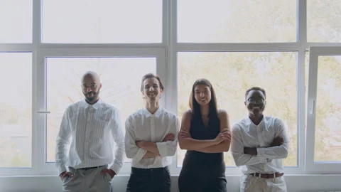 Four colleagues of different backgrounds stand by a window in an office. They 스톡 동영상 335734011