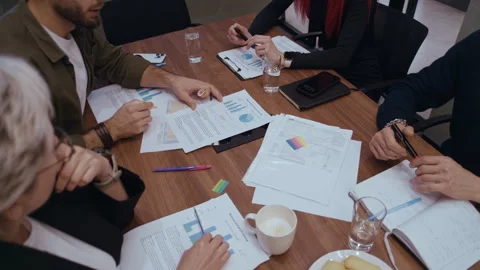 Four Colleagues Marking and Discussing Financial Performance Graphs Around Stock Footage 321017203