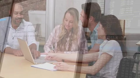 Four colleagues pointing at laptop and jotting notes around table reviewing code Stock Footage 330052720