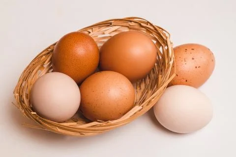 Four colored chicken eggs in a wicker brown basket and two eggs Stock Photos