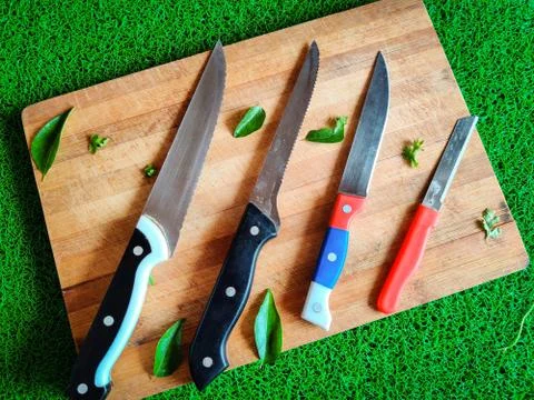 Four colored different sizes of knives kept on chopping board. With curry lea Stock Photos