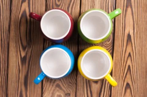 Four colored empty ceramic clean mugs on old worn brown wooden table Stock Photos