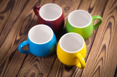 Four colored empty ceramic clean mugs on old worn brown wooden table Stock Photos