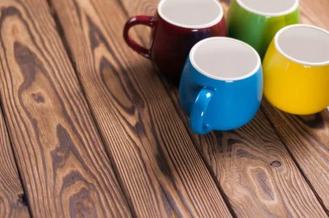 Four colored empty ceramic clean mugs on old worn brown wooden table Stock Photos
