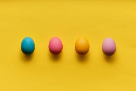 Four colorful easter eggs in a row on yellow paper with plenty of copy space Stock Photos