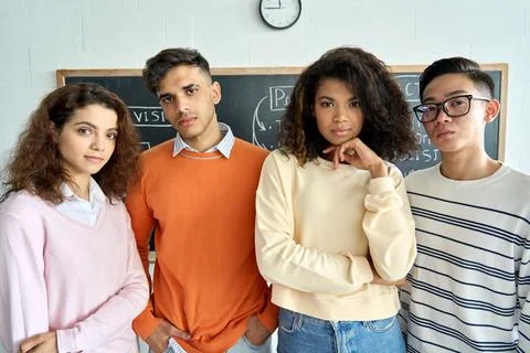 Four cool multiethnic students standing on black board background. Stock Photos
