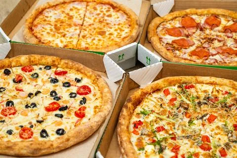 Four different cut pizzas are in square boxes. Meat and vegetarian pizza. Close Stock Photos
